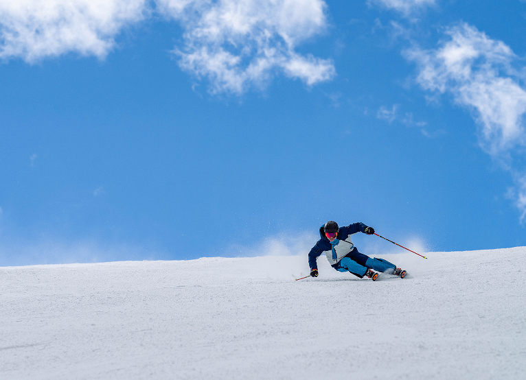 Single skier carves deeply down the mountain under blue skies