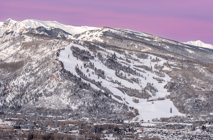 Pink skies over buttermilk mountain, snowy runs surrounded by snow capped pine trees