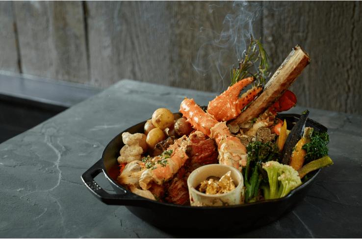 Plate of surf and turn, bone marrow, crab claw, season veggies all in a cat iron skillet at cloud 9