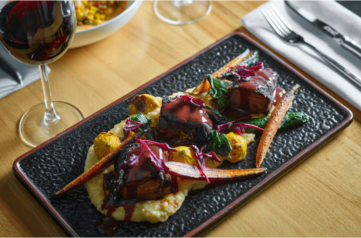 Seasonal roasted veggies on top of grits, glass of red wine above