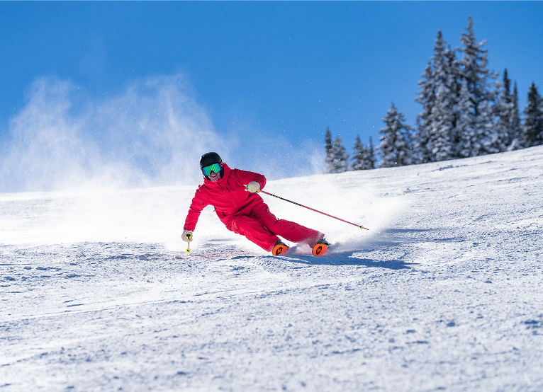 Skier in red ski suit carves down a white snowy hill, under blue skies on a spring day
