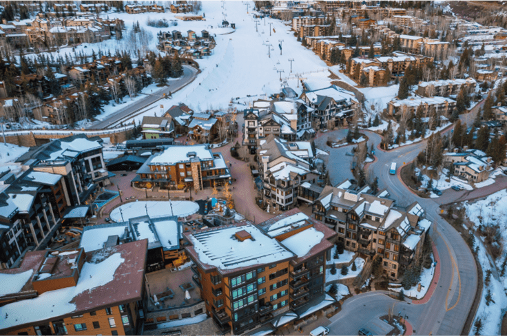 aerial view of Snowmass, road curves around tall hotels and the ski runs comes down to meet them