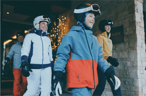 little boy smiles as he leads his family out of the parking garage at Limelight Snowmass, all are dressed in ski gear as they prepare to hit the slopes