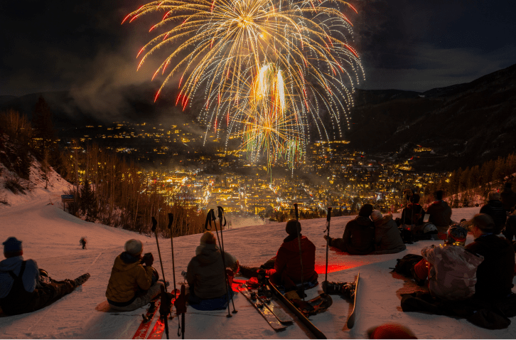 group sits atop aspen mountain on a winter night to watch the fireworks from above