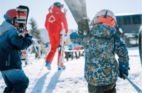 kids walk with skies on their shoulder at aspen