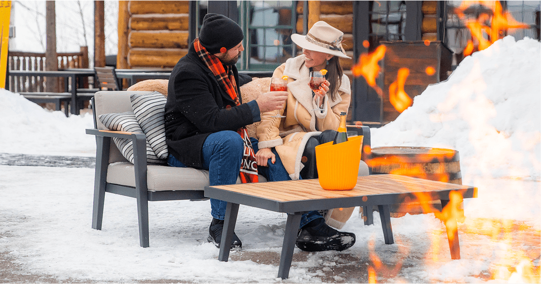 A husband and wife cheers their drinks in front of a fire at dusk at the snowcat experience at Snowmass's Cabin