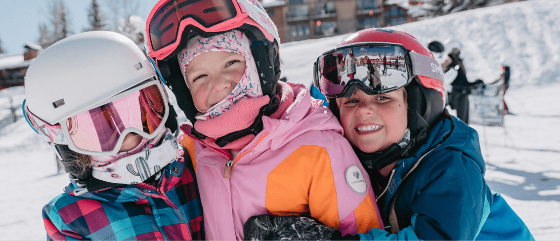 Thre kids hug each other on the slopes of aspen ski resort, smiling