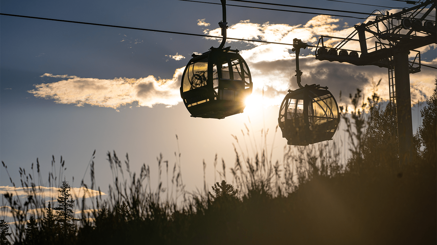 Two Gondola cars at dusk, sun is behind one car and shining through the windows and the grass in the foreground
